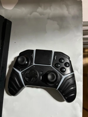 Nacon Revolution Pro PS4 handkontroll - Säljer en svart Nacon Revolution Pro handkontroll till PS4. Kontrollen har ergonomisk design, gummerade grepp och extra knappar för bättre spelupplevelse. Utrustad med touchpad, dubbla styrspakar och klassiska PlayStation-knappar. Perfekt för gaming.