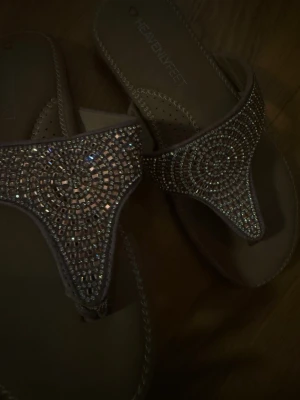 Beige glittriga sandaler  - Snygga beige sandaler från Heavenly Feet med T-rem design och massor av glittrande stenar i ett cirkelmönster. Mjuka sulor och dekorativa sömmar längs kanterna. 