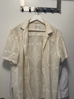 Vit virkad kortärmad kofta från Zara - Säljer en vit virkad kofta från Zara med korta ärmar och öppen front. Koftan har ett snyggt hålmönster och krage, perfekt att slänga över ett linne eller t-shirt.