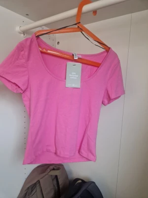 Rosa croppad topp med kort ärm - Snygg rosa croppad topp med korta ärmar och rundad urringning. Tillverkad av 25% återvunnen bomull, perfekt för dig som gillar en enkel men färgstark stil. Passar till både jeans och kjol för en trendig look.