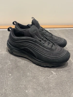 Nike Air Max 97 - Snygga Nike Air Max 97 i helsvart färg med ikoniska vågformade linjer och synlig Air Max-sula. Skorna har mesh och syntetmaterial för en sportig look och maximal komfort. Perfekta för dig som gillar streetwear och vill ha en stilren sneaker.