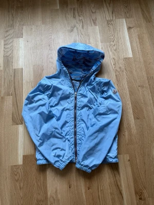 Moncler Vindjacka - Moncler vindjacka i modellen Gobert. Jackan går att vändas ut och in där ena sidan är ljusblå och andra sidan har camo mönster. Moncler loggan syns på båda sidorna och finns fickor på båda sidorna. Storlek 3 och är skicket är bra förutom små repor på ryggen som ej syns om man kollar nära.