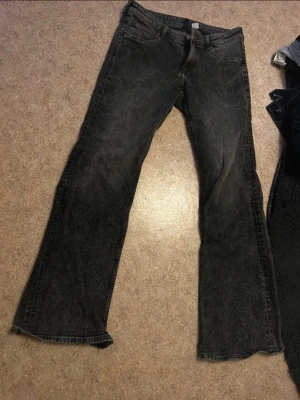 Svarta bootcut jeans med tvättad look - Ett par svarta bootcut jeans med lätt tvättad finish och klassisk femficksdesign. Jeansen har utsvängda ben och normal midja, perfekta för en avslappnad och trendig stil. Materialet är denim med en mjuk känsla.
