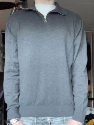 halvzip tröja - Snygg grå tröja från Jack & Jones med halv dragkedja och hög krage. Tröjan har långa ärmar, ribbade muddar och är tillverkad i ett mjukt material som passar perfekt till jeans. Enkel och stilren design som funkar till många outfits.