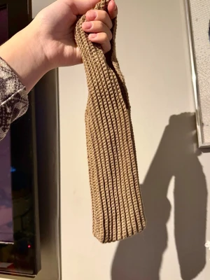 Virkad ribbad mobilpåse - En virkad mobilpåse i en neutral färg. Påsen har en enkel design med en strukturerad yta och ett handtag som är integrerat i väskans form. Den är kompakt och kan bäras runt väskremmen eller i handen. Använt några gånger och jag har fått plats med iPhone 17 PRO Max i den.