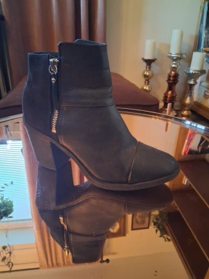 Svarta stövletter med dragkedja - Snygga svarta stövletter med grov klack och dragkedja på sidan. Skorna har en stilren design med rundad tå och är tillverkade i ett matt material som liknar mocka. Perfekta för att lyfta din outfit med en cool touch.