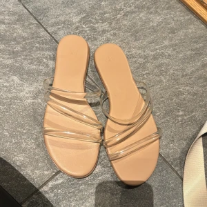 Beige sandaler med transparenta remmar - Säljer ett par stilrena sandaler från H&M med beige sula och flera transparenta plastremmar över foten. Helt oanvända 