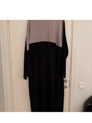 Svart och grå långklänning - En stilren långklänning i svart och ljusgrått blockmönster. Klänningen har lång ärm och rak passform, perfekt för dig som gillar enkel och modern design. Materialet känns mjukt och följsamt mot kroppen.