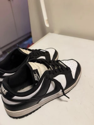 Nike Dunk Low Black/White – Stilren klassiker i fint skick - Säljer ett par Nike Dunk Low i den tidlösa black/white-färgställningen, storlek 44. En riktigt clean modell med vit bas, svarta detaljer och klassisk Swoosh – passar till i princip allt och funkar lika bra till vardag som till en mer uppstyrd streetlook.  Skorna är använda och har lite lätt creasing framtill (se bilder), men är överlag i bra skick. Sulorna är hela och stabila och skorna ger fortfarande ett snyggt helhetsintryck.  Perfekt för dig som vill ha ett par stilrena Dunks i strl 44 till 