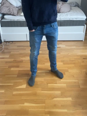 Blå slim fit jeans från Replay - Snygga blå slim fit jeans från Replay med klassisk femficksdesign och diskreta slitningar. Jeansen har normal midja och är tillverkade i stretchigt denim för en bekväm passform. Perfekta för en avslappnad och trendig look.