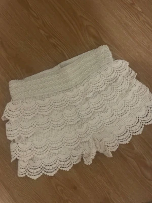 Vita spetsiga shorts med volang - Superfina vita shorts med flera lager volang i spets. De har en bred, elastisk midja som gör dem bekväma och sitter snyggt på plats. Perfekta för varma sommardagar och ger en romantisk vibe till din outfit.