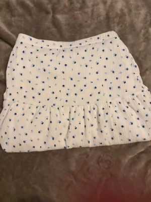 Vit kortkjol med blå prickar Kappahl - Supersöt vit kortkjol från Kappahl med blå prickigt mönster och volang nedtill. Kjolen är gjord i ett mjukt bomullstyg och har en bekväm resår i midjan. Perfekt för dig som gillar en lekfull och fräsch stil.