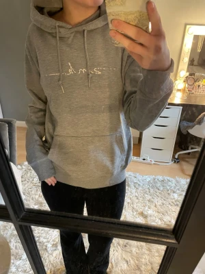 Grå hoodie med broderad text - Snygg grå hoodie från Zink med vit text på bröstet. Hoodien har huva med dragsko, magficka och ribbade muddar vid ärmslut och nederkant. Perfekt för en avslappnad och trendig stil. Ej bra pris,, skriv. Sitter som Xs,S,M, lång. Trycket försvinner allt efter som. 