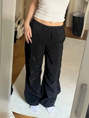 Svarta vida leggings med dragsko - Säljer ett par svarta leggings med lös passform och dragsko i midjan. Byxorna har raka, vida ben och är tillverkade i ett lätt och mjukt material som ger en avslappnad look. Perfekta för en chill och trendig stil.