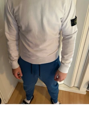 Vit tröja från Stone Island - Vit tröja från Stone Island med rund halsringning och ribbade muddar vid ärmslut och nederkant. Tröjan har den klassiska Stone Island-loggan på vänster ärm och är enkel men stilren i designen.