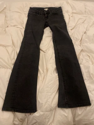 Svarta bootcut jeans med fickor - Snygga svarta bootcut jeans med klassiska fem fickor och låg midja. Jeansen har utsvängda ben och är tillverkade i ett stretchigt denimtyg som ger en bekväm passform. Perfekta för dig som gillar en retroinspirerad stil.