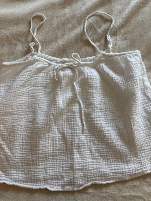 Vit topp från med knyt/rosett - Superfin vit linnetopp från H&M med tunna axelband och knyt framtill. Mycket skön och luftig, perfekt för varma dagar🤍Är i storlek Xs men hade passat S lika bra!