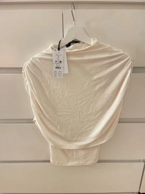 Topp från Gina Tricot  - Superfin vit topp från Gina Tricot i storlek S. Helt ny med prislapp kvar. Modell: Cape ruched top. Nypris är 279kr Den är aldrig använd. Hör av er vid frågor eller prisförslag💕