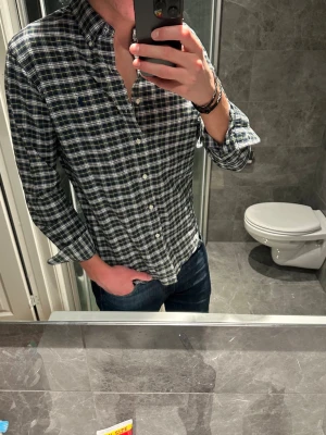 Ralph lauren flanellskjorta  - Snygg rutig skjorta i svart, vit och grön från Ralph Lauren. Funkar året runt. Skjortan är i riktigt bra skick och har inga tecken på användning. Jag på bilden är 188cm och bör storlek S. Hör av er vid fler frågor eller eventuella prisförslag:)