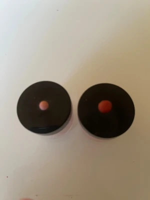 Ackryl i burk med svart lock - Två burkar med lösrouge i puderform, båda med svart lock och transparent burk. Färgerna är ljusrosa och persikorosa, vilket ger en fräsch och naturlig look till kinderna. Perfekt för att bygga upp färgintensitet och lätt att applicera med borste.