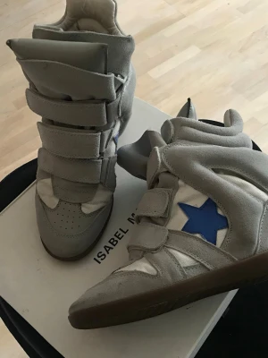 Isabel Marant Willow sneakers i grå, storlek 38 - Isabel Marant Willow sneakers med kardborreband. Skorna har en dold kilklack och en blå stjärna på sidan. Yttersulan är i gummi.