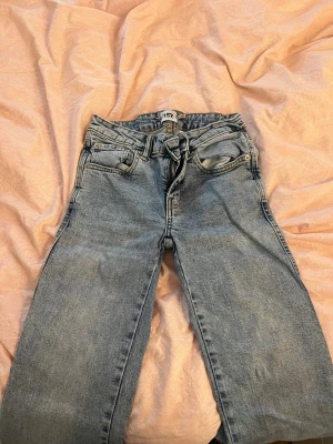 Blå raka jeans från 157 - Ett par klassiska blå jeans från 157 med utsvängda ben och medelhög midja. Jeansen har 4 fickor, bälteshällor och snygga detaljer på bakfickorna med knappar. Tillverkade i denim med en ljus tvätt som ger en avslappnad look.