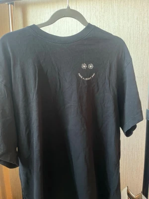 Svart t-shirt med tryck - Svart t-shirt i bomull med små blommor och texten 'Have a lovely day' tryckt på bröstet. Väldigt stor i storleken.