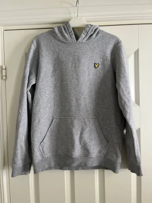 Grå hoodie från Lyle & Scott - Snygg grå hoodie från Lyle & Scott med gul logga på bröstet. 