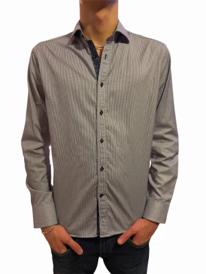 Skjorta  - Snygg blå skjorta med smala vertikala ränder och svarta knappar. Klassisk krage och långärmad modell, perfekt till jeans. Skjortan har en stilren look och är tillverkad i bomull för skön känsla.