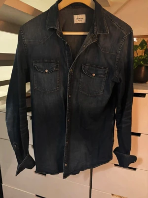 Dondup Westernshirt  - Snygg mörkblå jeansskjorta från Dondup med två bröstfickor och tryckknappar. Skjortan har klassisk krage, långa ärmar och detaljerad söm samt ett broderat D på ärmslutet. Perfekt för en avslappnad men stilren look. Har satt storlek medium fastän att den är en XL. Eftersom att den är väldigt trång och liten!