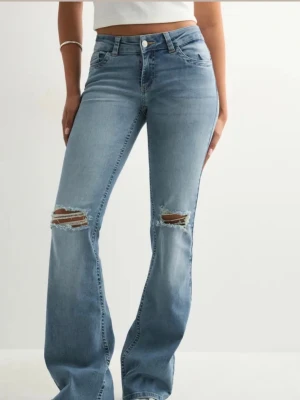 Jeans Nelly  - Säljer ett par ljusblå bootcut jeans med slitna detaljer över knäna. Jeansen knäppning på baksida fickor. Jeansen är i storlek 32 och som referens har jag vanligtvis xs och är 160 lång. Säljer då de inge kommer till användning men de är som nya.
