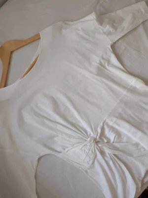 Vintage Vit twistad topp från Mango - Snygg vit topp från Mango med twistad detalj framtill. Tillverkad i mjukt bomullsmaterial och har korta ärmar samt rund halsringning för en off the shoulder look. Perfekt att styla med jeans eller kjol. Är i storlek L men passar som en oversized look. Jag brukar ha s-m. 