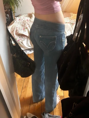 Blå low waist bootcut jeans levi’s - Säljer ett par ljusblå low waist jeans med bootcut passform och dubbla knappar fram. Jeansen har dekorativa sömmar på bakfickorna och är i klassisk denim. Perfekta för en avslappnad och trendig look. Passar en xs och xxs