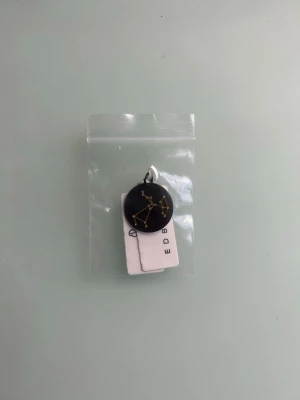 Edblad berlock med skytten  - Unikt halsband från Edblad med en rund svart berlock som har sjärntecknet skytten i guldfärg. Berlocken är ungefär lika stor som en 2 krona, hänger i en enkel ögla och passar perfekt för dig som gillar astrologi och personliga smycken. Snygg detalj till din outfit. Aldrig använd och tror inte ens den har blivit öppnad. Säljer eftersom jag inte är skytt💗