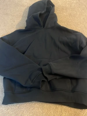 Mörkblå hoodie med huva - En klassisk mörkblå hoodie med huva och ribbade muddar. Hoodien har en relaxed passform och är perfekt för en chill vardagslook. Tillverkad i mjukt material som känns skönt mot huden. Storlek XS