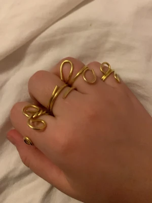 Guldiga statementringar i metalltråd - Unika ringar i guldig metalltråd med lekfulla, abstrakta former. Perfekta för dig som vill sticka ut och addera en konstnärlig touch till din stil. Säljs som set och passar flera fingrar samtidigt.
