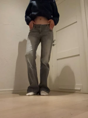 Ljusgrå bootcut jeans med låg midja - Säljer ett par ljusgrå jeans med bootcut passform och låg midja. Jeansen har klassiska fem fickor och stängs med dragkedja och knapp. Perfekta för en avslappnad och trendig look. Materialet är denim i bomull.