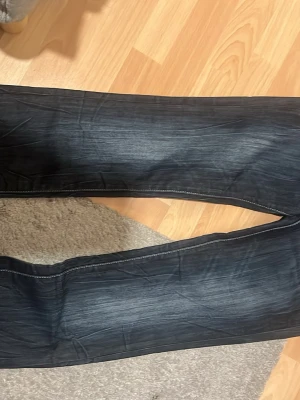Mörkblå bootcut jeans från Guess - Snygga mörkblå bootcut jeans från Guess med kontrastsömmar och klassiska fem fickor. Jeansen har en diskret tvättad look och en liten metallogo på bakfickan. Perfekta för dig som gillar en tidlös och stilren denimstil.