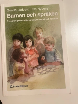 Barnen och språken kursbok - Kurslitteratur med titeln 'Barnen och språken' av Gunilla Ladberg och Ola Nyberg. Boken har ett omslag i gröna och beige toner med illustration av barn. Den handlar om tvåspråkighet och flerspråkighet i familj och förskola.