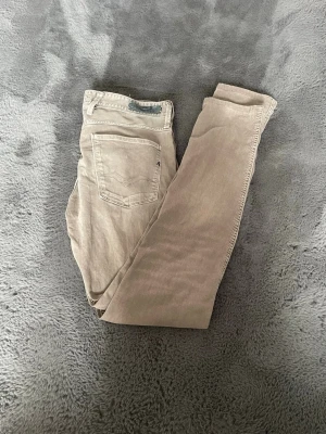 Beige raka jeans från Replay  - Säljer ett par beige jeans från Replay med klassisk femficksdesign och raka ben. Jeansen har diskreta sömmar på bakfickorna och en liten Replay-logga vid fickan. Perfekta för en avslappnad och stilren look.