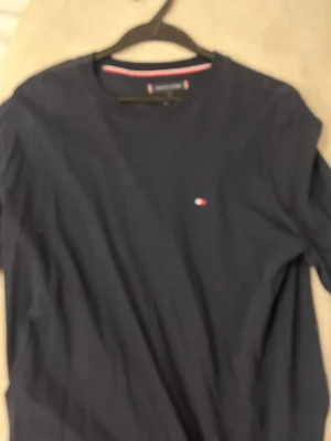 Mörkblå tunn långärmad tröja från Tommy Hilfiger - Snygg mörkblå t-shirt från Tommy Hilfiger med klassisk rund hals och diskret logga på bröstet. Tillverkad i mjuk bomull som känns skön mot huden. Perfekt för en clean och stilren look.