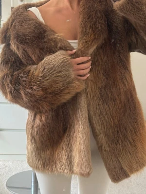 Brun pälsjacka - Snygg brun pälsjacka. Jackan har en klassisk rak passform och stängs framtill. Perfekt för att hålla värmen under kalla dagar och ger en lyxig känsla till din outfit. Sitter perfekt och är väldigt snygg och tidlös! Den är köpt vintige! Älskar den men har redan många andra, priset kan diskuteras vid snabb affär!