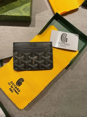 Svart kortfodral - Snyggt svart kortfodral med det klassiska mönstret i vitt och grått. Tillverkat i exklusivt läder med flera fack för kort. Perfekt accessoar för dig som vill ha något stilrent och lyxigt i fickan.