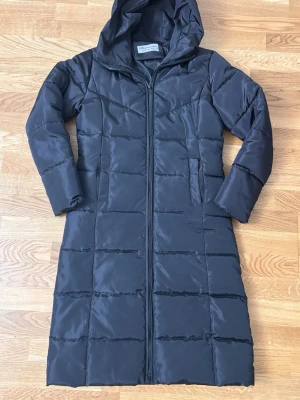 Svart lång dunjacka med huva - Lång vinterjacka stl M – Meishangnvhai             Varm jacka med huva, fint skick. Upplevs lite tight – jag har normalt stl S och byst 80D. 