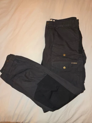 Svarta G-1000 byxor Fjällräven - Fjällräven friluftsbyxor – Mörkgrå/svart (50) Friluftsbyxor från Fjällräven i mörkgrått. Storlek: 50 Skick: Bra begagnat skick. Anmärkning: Lite slitage längst ner på ena benet, inget större.