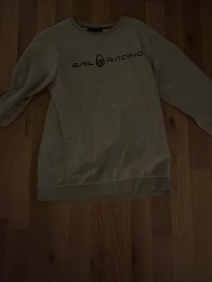Grå sweatshirt från Sail Racing - Snygg grå sweatshirt från Sail Racing med svart logga tryckt över bröstet. Den är 160 cm storlek, men den passar fortfarande mig bra och jag är 175 cm
