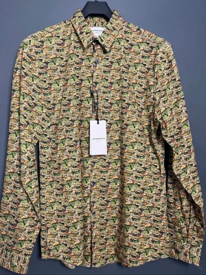Mönstrad skjorta från Lindbergh - Färgstark skjorta från Lindbergh med ett unikt tiger- och djungelmönster i grönt, gult, svart och orange. Skjortan har klassisk krage, knappar framtill och långa ärmar. Perfekt för dig som vill sticka ut med en cool och lekfull stil.