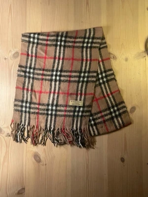 Burberry rutiga halsdukar i ull - 50 procent rea nu från 600kr till 300 in o köp.Två klassiska halsdukar från Burberry i ull med det ikoniska rutmönstret. En i beige med svarta, vita och röda rutor, och en i mörkgrönt med samma mönster. Båda har fransar i ändarna och en liten Burberry-etikett.300kr st