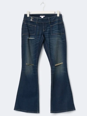 Mörkblå bootcut jeans med slitningar - Säljer ett par mörkblå bootcut jeans med slitna detaljer över knäna och stora framfickor. Jeansen har låg midja och två knappar i linningen för extra detalj. Materialet är klassisk jeans i bomull och passformen är loose nertill med en snygg utsvängd siluett.