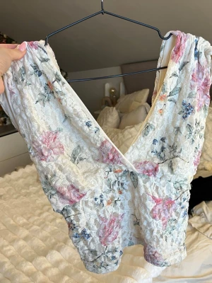 Blommig spetsblus med v-ringning - Supersöt blus i ljus spets med blommigt mönster. Djup v-ringning framtill och ärmlös design ger en romantisk vibe. Perfekt att styla med jeans eller kjol inför sommaren💓